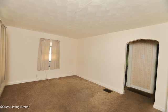 carpeted empty room with visible vents, baseboards, and arched walkways