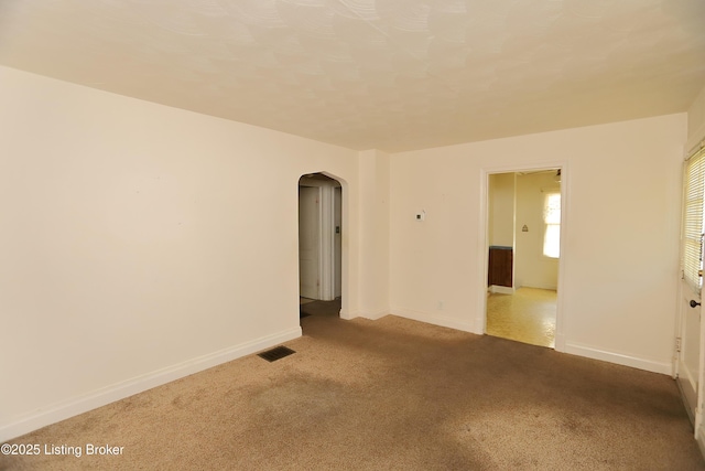 carpeted spare room featuring baseboards, visible vents, and arched walkways