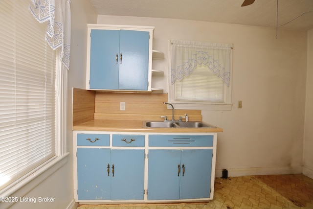 kitchen featuring open shelves, a sink, light countertops, baseboards, and blue cabinetry