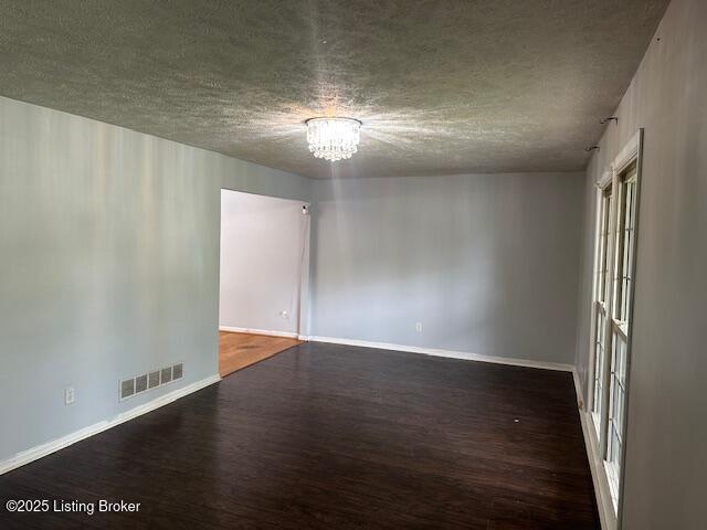 unfurnished room featuring a textured ceiling, visible vents, baseboards, wood finished floors, and a notable chandelier