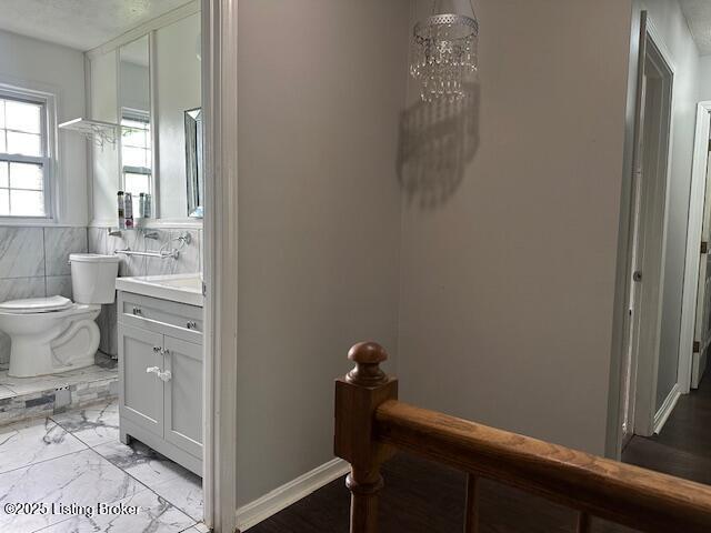 bathroom featuring marble finish floor, toilet, vanity, baseboards, and a notable chandelier