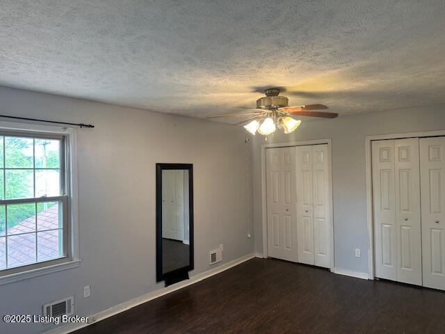 unfurnished bedroom featuring a textured ceiling, baseboards, multiple closets, and dark wood-type flooring