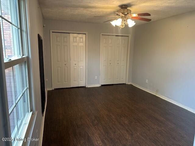 unfurnished bedroom featuring multiple windows, baseboards, multiple closets, and dark wood finished floors