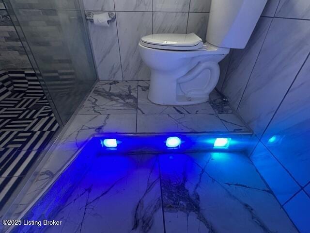 full bath with toilet, a shower stall, marble finish floor, and tile walls
