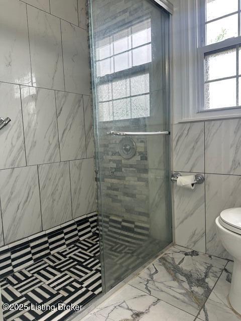 bathroom with toilet, marble finish floor, tile walls, and a shower stall