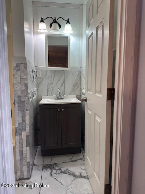 bathroom with marble finish floor, tile walls, and vanity