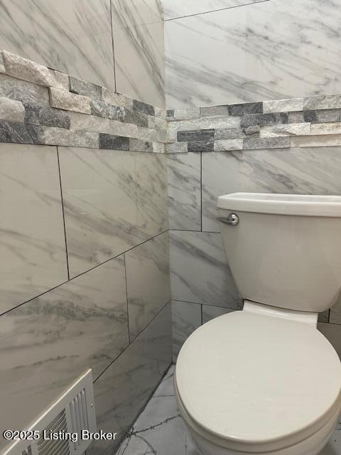 bathroom with toilet, marble finish floor, and tile walls