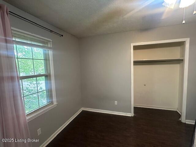 unfurnished bedroom with a textured ceiling, wood finished floors, a closet, and baseboards
