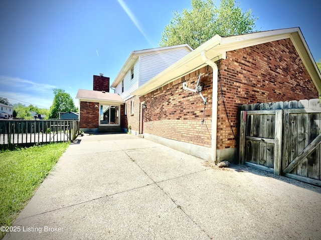 view of property exterior featuring a chimney, brick siding, and fence