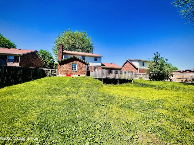 rear view of house featuring a chimney, a yard, brick siding, and a fenced backyard