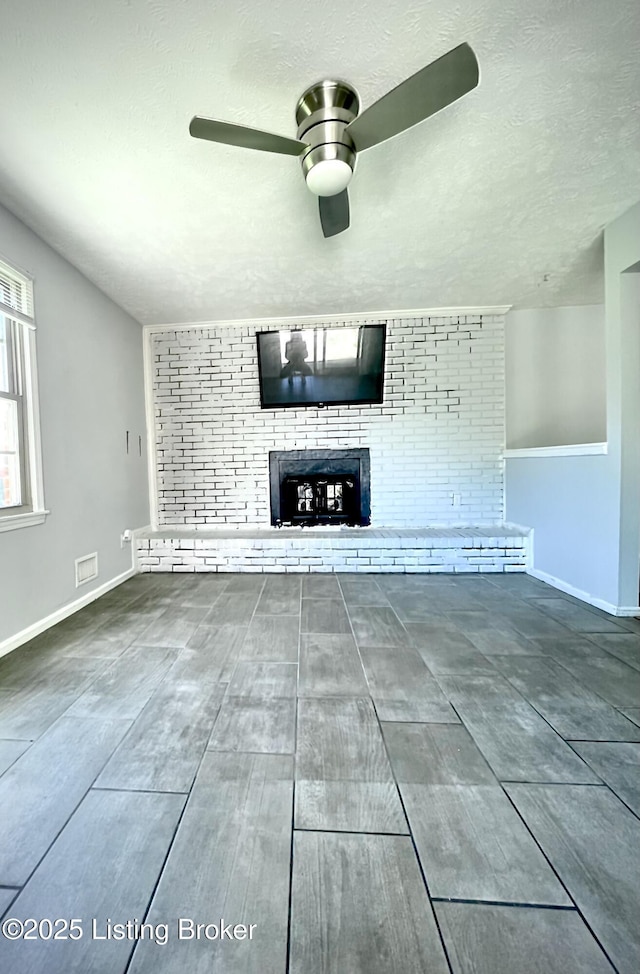 unfurnished living room with a fireplace, a ceiling fan, visible vents, baseboards, and a textured ceiling