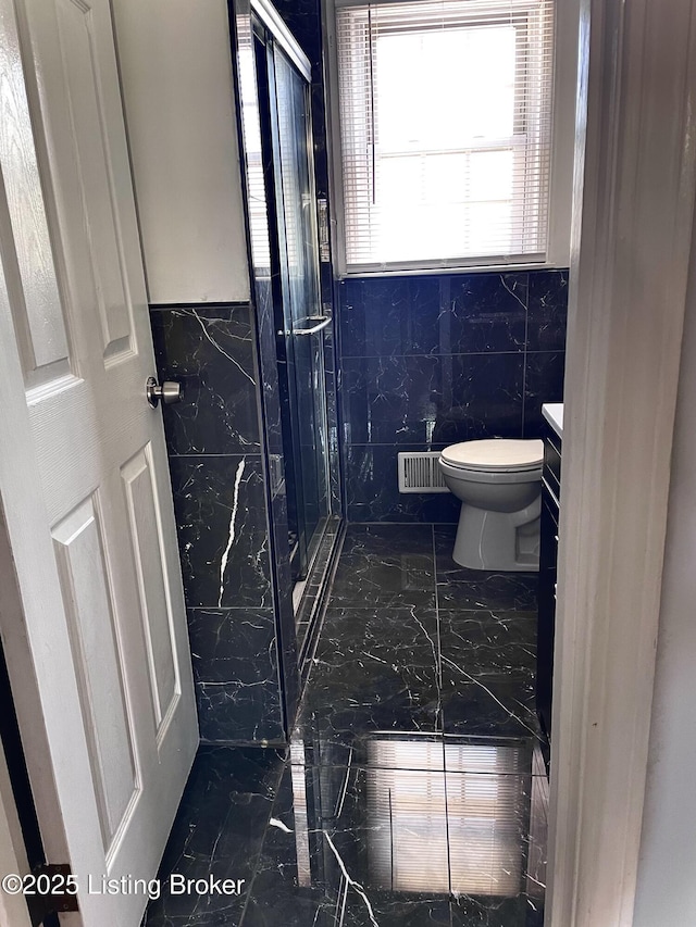 bathroom with tile walls, a shower stall, toilet, marble finish floor, and visible vents