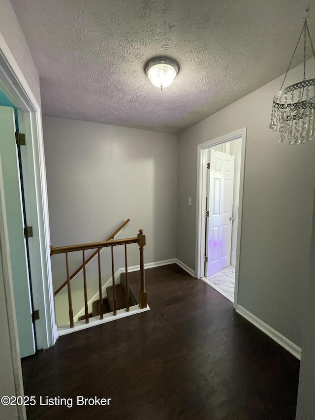 hall featuring a textured ceiling, an upstairs landing, baseboards, wood finished floors, and a notable chandelier