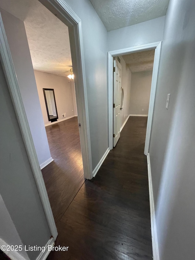 hall featuring a textured ceiling, wood finished floors, and baseboards