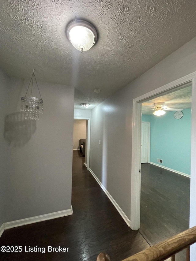 hallway featuring a textured ceiling, wood finished floors, and baseboards