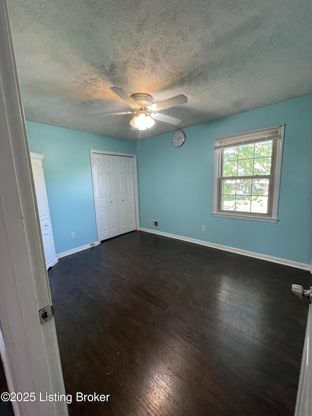 unfurnished bedroom with a textured ceiling, visible vents, dark wood-style floors, and baseboards