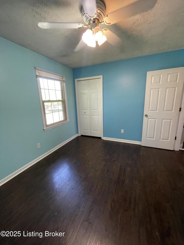 unfurnished bedroom featuring a textured ceiling, baseboards, dark wood-style floors, and a closet
