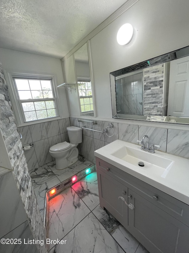 bathroom with tile walls, toilet, a textured ceiling, and marble finish floor