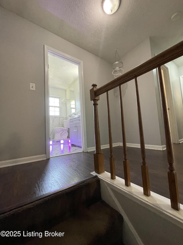 staircase featuring an inviting chandelier, a textured ceiling, wood finished floors, and baseboards