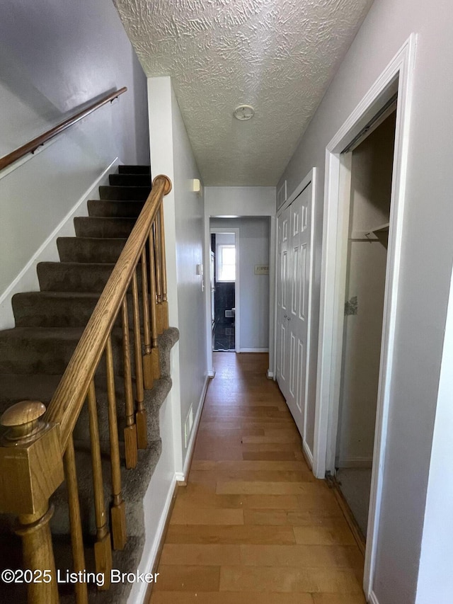 corridor featuring wood finished floors, stairway, baseboards, visible vents, and a textured ceiling