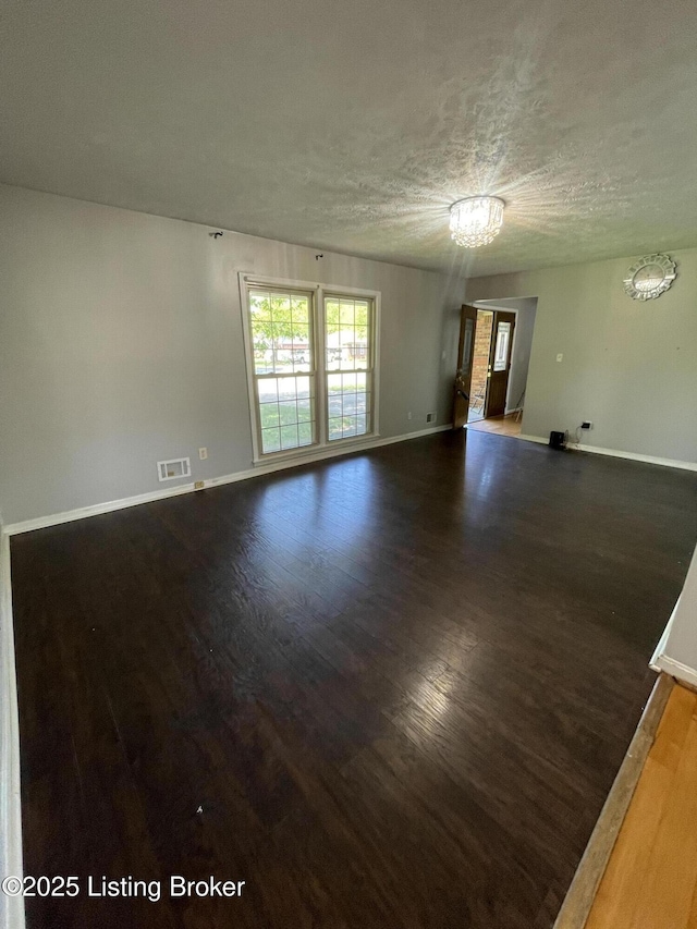 spare room featuring a textured ceiling, visible vents, baseboards, and dark wood-type flooring