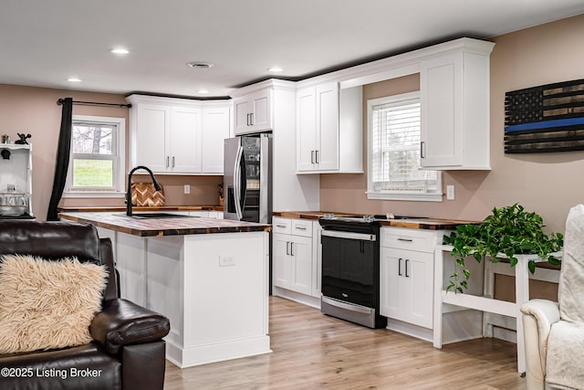 kitchen featuring wood counters, stainless steel appliances, white cabinets, light wood finished floors, and a sink