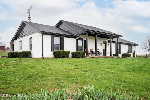 back of property featuring a porch, a lawn, roof with shingles, and brick siding