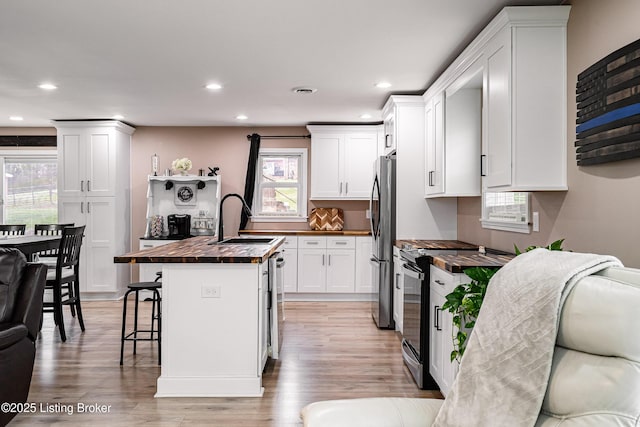 kitchen featuring recessed lighting, wood counters, stainless steel appliances, a kitchen bar, and a sink