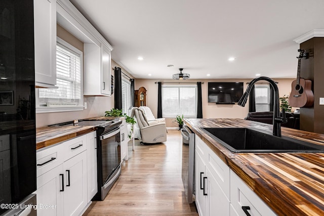 kitchen with recessed lighting, light wood-style floors, wooden counters, a sink, and open floor plan