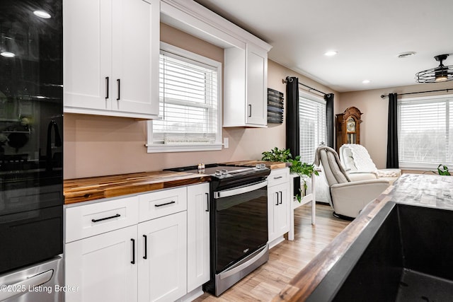 kitchen featuring light wood finished floors, wood counters, stainless steel electric range, black fridge, and white cabinets