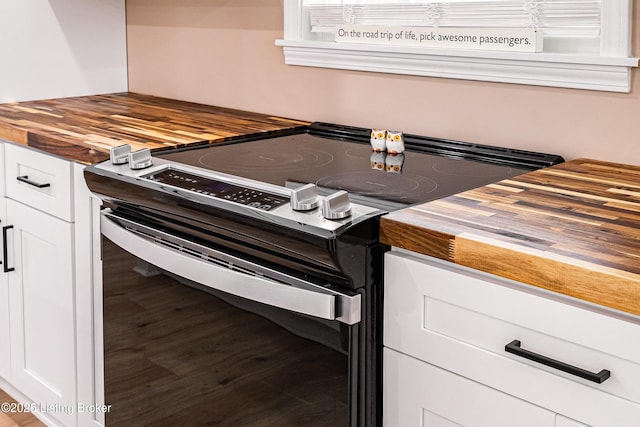 room details with butcher block counters, white cabinetry, wood finished floors, and stainless steel range with electric cooktop