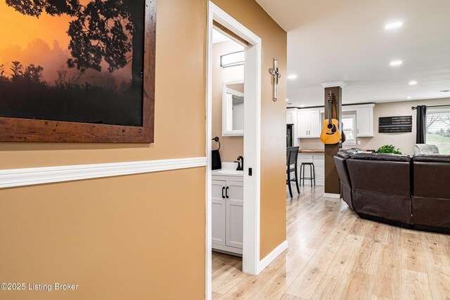 hallway with light wood-type flooring, recessed lighting, and a sink