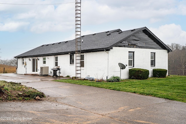 view of property exterior featuring central AC, roof with shingles, a yard, and brick siding