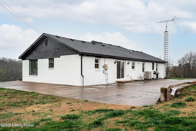 rear view of property with a yard, a patio area, central air condition unit, and brick siding