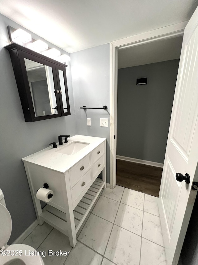 half bathroom with baseboards, toilet, vanity, and marble finish floor