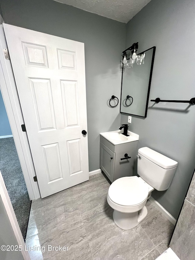 bathroom with toilet, a textured ceiling, vanity, and baseboards