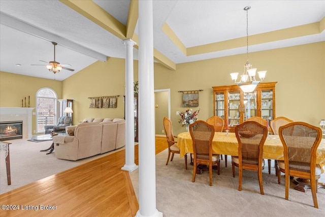 dining space featuring decorative columns, vaulted ceiling with beams, a glass covered fireplace, light carpet, and ceiling fan with notable chandelier