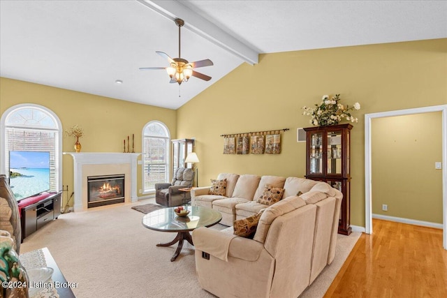 living area with a fireplace with flush hearth, ceiling fan, lofted ceiling with beams, and plenty of natural light