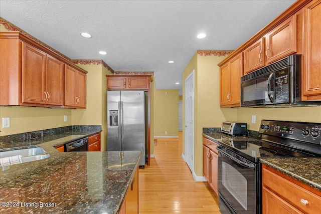 kitchen featuring dark stone countertops, a sink, black appliances, light wood-type flooring, and recessed lighting