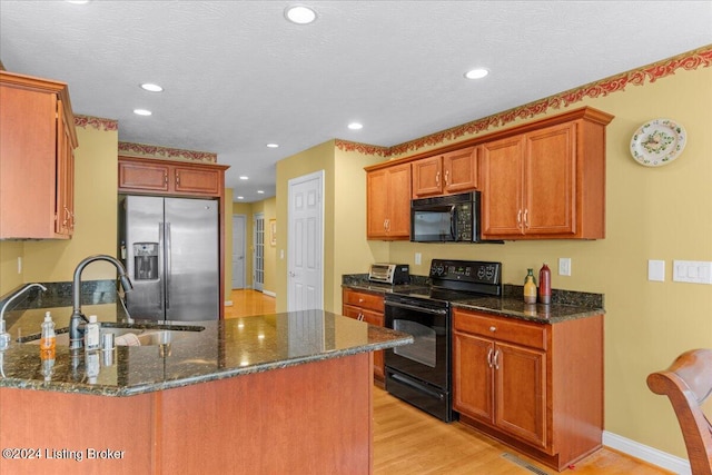 kitchen featuring dark stone counters, light wood finished floors, a sink, black appliances, and a peninsula
