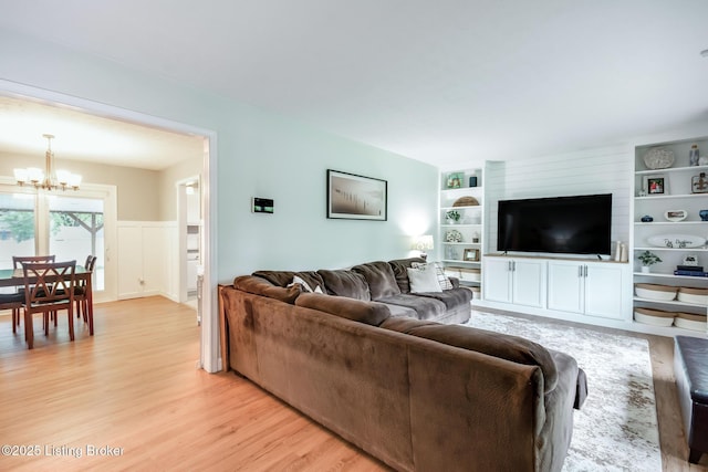 living room featuring a notable chandelier, wainscoting, built in features, and light wood-style floors