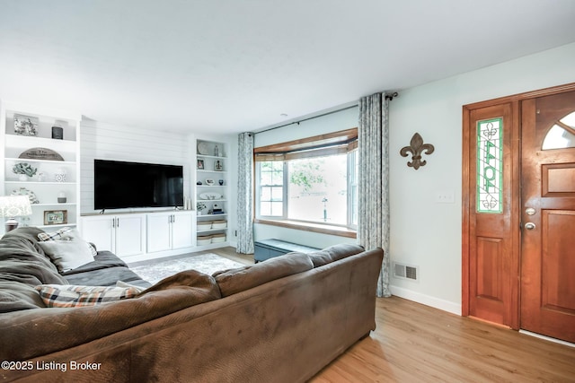 living area with baseboards, visible vents, built in features, and light wood-style flooring