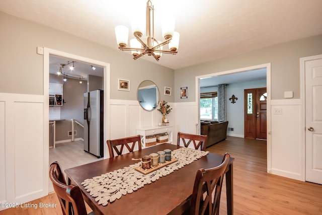 dining area featuring light wood-style floors, a decorative wall, a notable chandelier, and wainscoting