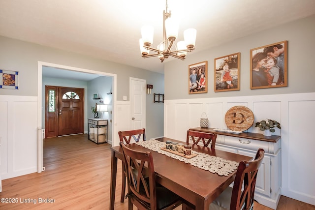 dining space with light wood-type flooring, a wainscoted wall, a notable chandelier, and a decorative wall