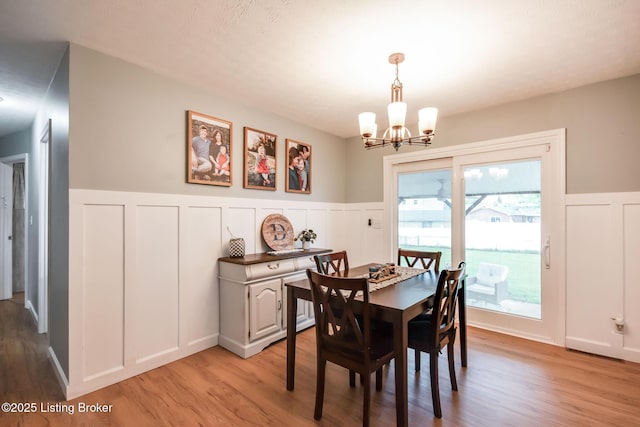 dining room featuring light wood finished floors, a decorative wall, a notable chandelier, and wainscoting