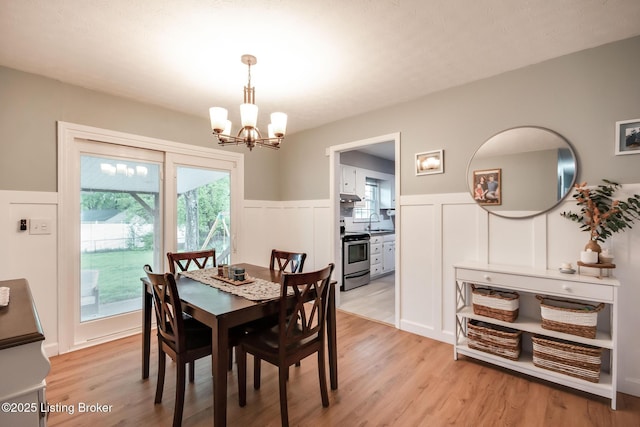 dining area featuring a wainscoted wall, an inviting chandelier, light wood-style flooring, and a decorative wall