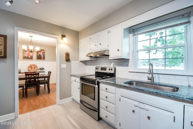 kitchen featuring dark stone countertops, stainless steel range with electric cooktop, a chandelier, under cabinet range hood, and a sink
