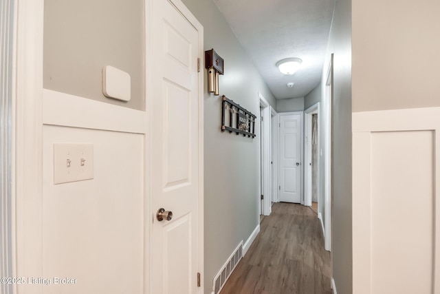 corridor featuring wood finished floors, visible vents, and baseboards