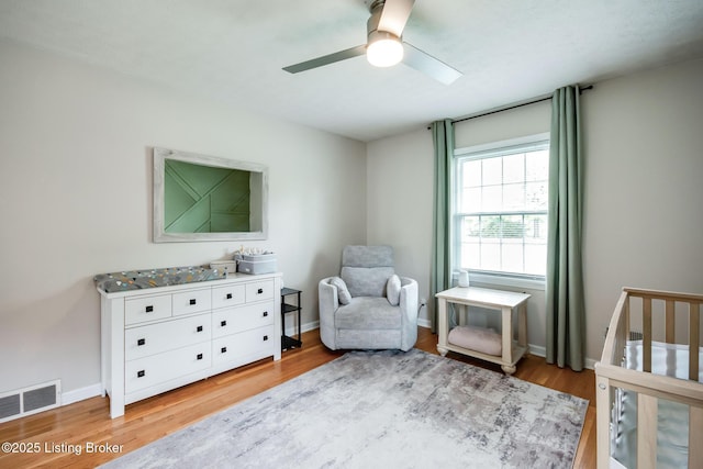 bedroom with light wood-style floors, a ceiling fan, visible vents, baseboards, and a crib