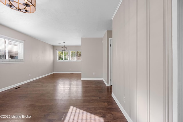 unfurnished living room with visible vents, a notable chandelier, baseboards, and dark wood-type flooring
